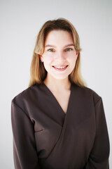 Smiling young woman in brown medical uniform on white background.