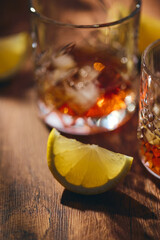 Glasses of whiskey with ice and lemon slices on wooden table in the rays of light. Shallow depth of field, close up.