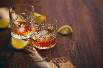 Glasses of whiskey with ice and lemon slices on a wooden table in the rays of light. Shallow depth of field