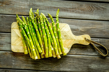 Cooking asparagus. Fresh steams on cutting board on dark wooden background top-down