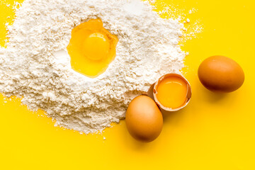 Making dough concept. Pile of flour and eggs on yellow background top view