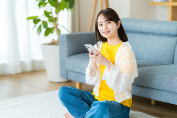 部屋でスマホを操作する若い女性