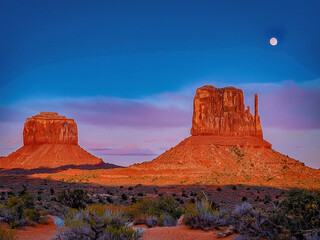 Evening light and full moon over iconic desert cliffs and dry wilderness
