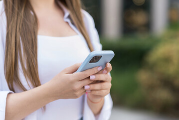 Close-up of a young woman's hands using a mobile phone while walking outdoors in the city....
