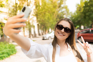 Attractive young woman in casual clothes and sunglasses taking a selfie photo on mobile phone...