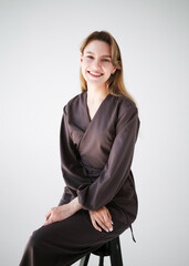 Smiling female doctor in brown uniform sitting on a stool in studio with white background and copy...