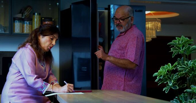 Indian couple making grocery list at home, Asian wife writing on notepad while husband checks refrigerator and tells food items to be ordered, planning weekly shopping household kitchen essentials - Powered by Adobe