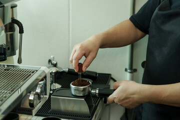 Closeup male barista using tool to level coffee grounds at espresso machine inside cafe, showing artisan precision, dedication, and care of small family coffee business, Concept small business
