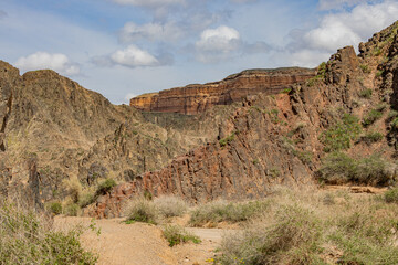 Charyn Canyon landscape with rugged cliffs, dry grass, and dramatic rock formations under a blue sky