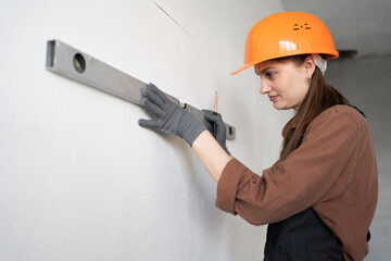 Serious woman builder in hardhat doing measures with spirit level on the wall