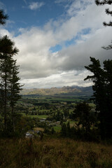 This captivating image captures a scenic view from Conical Hill in Hanmer Springs, New Zealand, showcasing a lush green valley nestled between rolling hills and distant mountains.