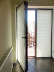 Glass door fitted with pleated blinds, partially open to a small balcony. The pleated shades is ideal for doors, as it takes up minimal space and allows the door to open wider for better access.