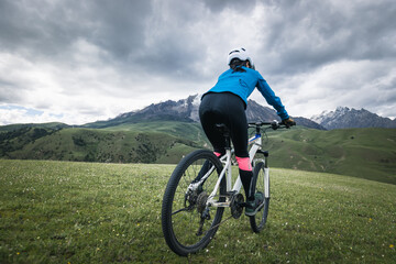 Woman cyclist riding mountain bike on grassland mountains with snow capped mountain in the distance
