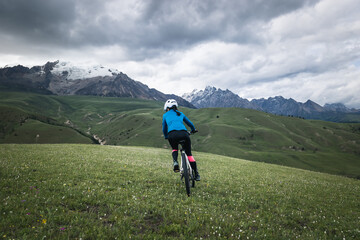 Woman cyclist riding mountain bike on grassland mountains with snow capped mountain in the distance