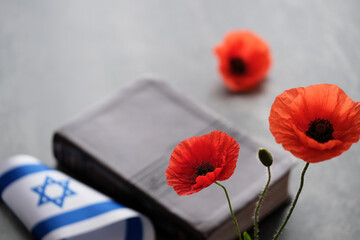 Bright red poppies arranged next to a closed book adorned with an Israeli flag. War memorial...