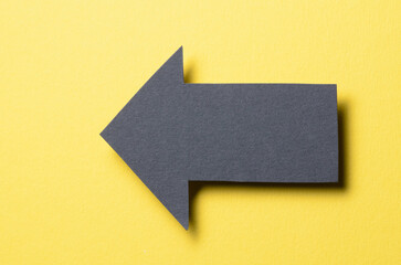 Black cut out blank paper cardboard arrow direction sign with copy space for text on yellow background, flat lay top view pointing symbol conceptual message backdrop