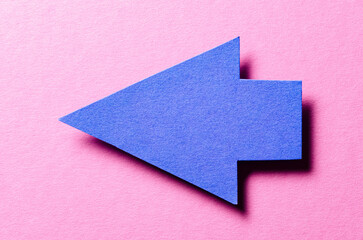 Blue cut out blank paper cardboard arrow direction sign with copy space for text on pink background, flat lay top view pointing symbol conceptual message backdrop