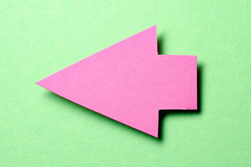Pink cut out blank paper cardboard arrow direction sign with copy space for text on green background, flat lay top view pointing symbol conceptual message backdrop