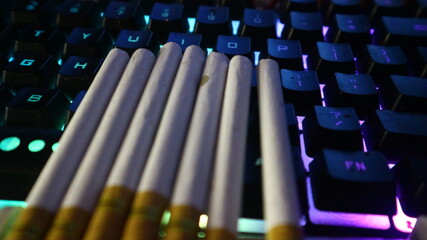 Cigarettes resting on a vibrant RGB backlit gaming keyboard, creating a modern and moody...