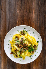 Papperdelle pasta with champignons mushrooms in cream sauce and parsley on wooden table