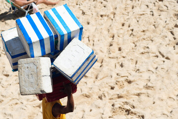 A worker at Porto da Barra beach is seen on the sand carrying material during strong sunlight. City of Salvador, Brazil.