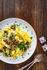 Papperdelle pasta with champignons mushrooms in cream sauce and parsley on wooden table