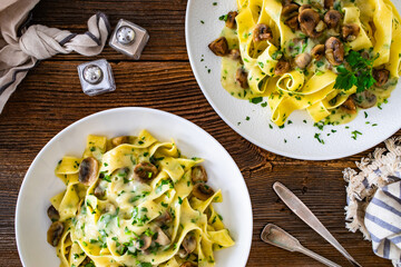 Papperdelle pasta with champignons mushrooms in cream sauce and parsley on wooden table