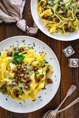 Papperdelle pasta with champignons mushrooms in cream sauce and parsley on wooden table