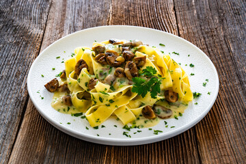 Papperdelle pasta with champignons mushrooms in cream sauce and parsley on wooden table