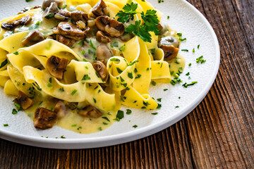 Papperdelle pasta with champignons mushrooms in cream sauce and parsley on wooden table