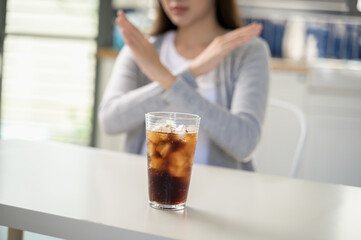 A person makes a hand gesture to refuse a glass of soda with ice. This concept highlights healthy...