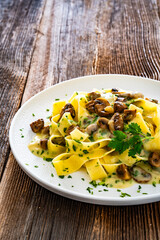 Papperdelle pasta with champignons mushrooms in cream sauce and parsley on wooden table