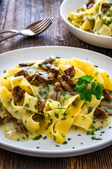 Papperdelle pasta with champignons mushrooms in cream sauce and parsley on wooden table