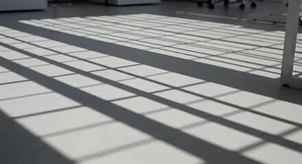 Sunlight streams through a window casting geometric shadows on a light-grey floor, creating an abstract pattern of light and shadow.