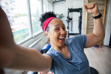 Happy senior woman taking post workout selfie at gym flexing arm