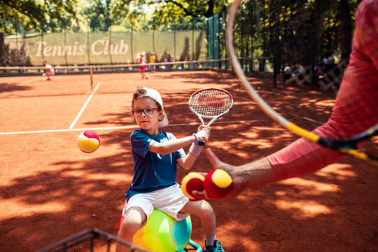 Young boy learning tennis at summer camp on clay court