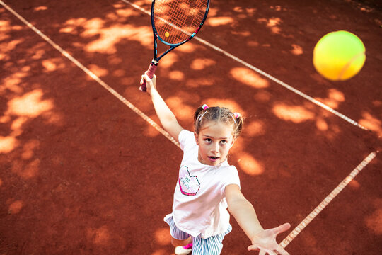 Young girl playing tennis on clay court during summer practice