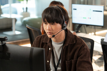 Focused customer support representative wearing headset works at computer in modern office...