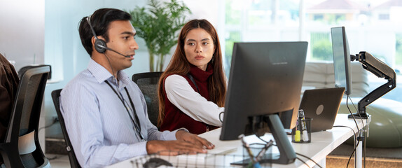 Two customer support professionals are working modern office environment. One is wearing headset...