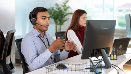 Professional tech support representative wearing headset is assisting customer while working at modern office desk with computer. colleague is seated nearby, focused on her tasks