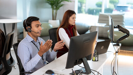 Customer support team working in modern office environment, with male agent wearing headset and...