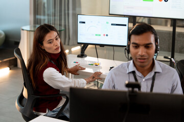 Two professionals are working modern tech customer support office. man wearing headset is focused his computer screen, while woman looks another monitor displaying analytics. environment