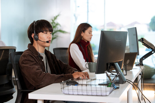 Two customer support representatives are working their desks modern office. man foreground is wearing headset and focused his computer screen, while woman background is also engaged her work