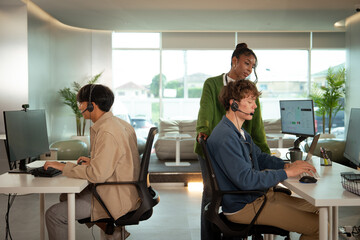 Team of tech customer support professionals working in modern office, wearing headsets and engaging...