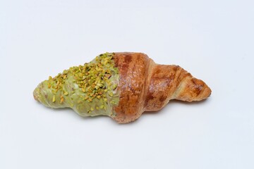 Top view of gourmet pistachio croissant with green glaze and crushed pistachio nuts on white background.