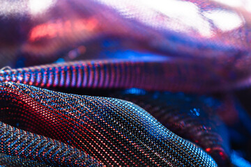 Close-up of shimmering metallic fabric with red, blue, and purple reflections, abstract folds, and...