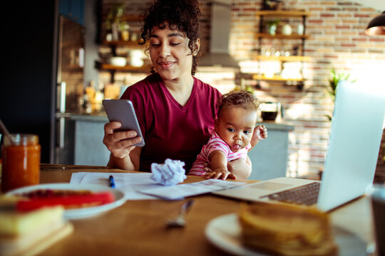 Work from home mom with baby on video call in kitchen
