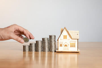 Close-up of hand collecting money with small house model, symbolizing saving for future home...