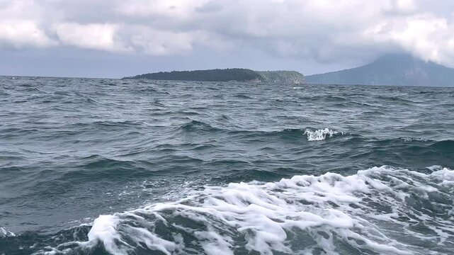 Anak Krakatau view in Lampung Indonesia. Dark glowing clouds above the open sea and evergreen forest. Dramatic sky, epic seascape. A view from the yacht. Nature, environment, climate change