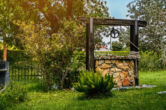 Beautiful artesian well made by stones and wheel pulley with metal bucket and rope in peaceful garden atmosphere. Retro stone water well in rural area. Garden decoration with antique items.